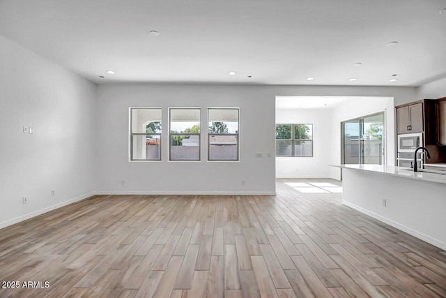 unfurnished living room featuring a sink, light wood-type flooring, baseboards, and recessed lighting