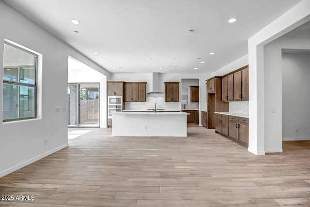 kitchen featuring recessed lighting, built in microwave, wall chimney exhaust hood, light wood-type flooring, and backsplash