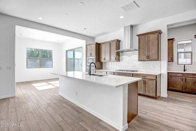 kitchen featuring visible vents, wall chimney range hood, light wood-style floors, stainless steel gas stovetop, and a sink