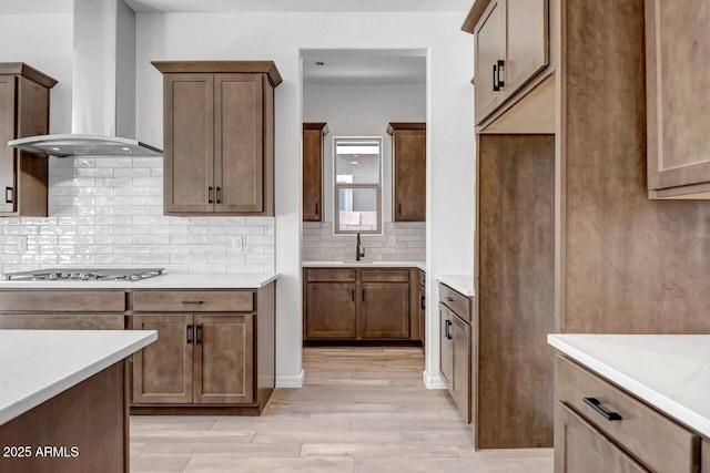 kitchen featuring light wood-type flooring, light countertops, decorative backsplash, wall chimney exhaust hood, and a sink