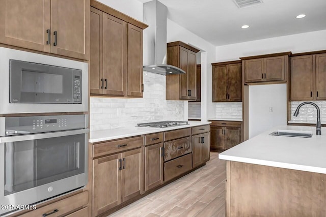 kitchen with ventilation hood, light wood-type flooring, light countertops, appliances with stainless steel finishes, and a sink