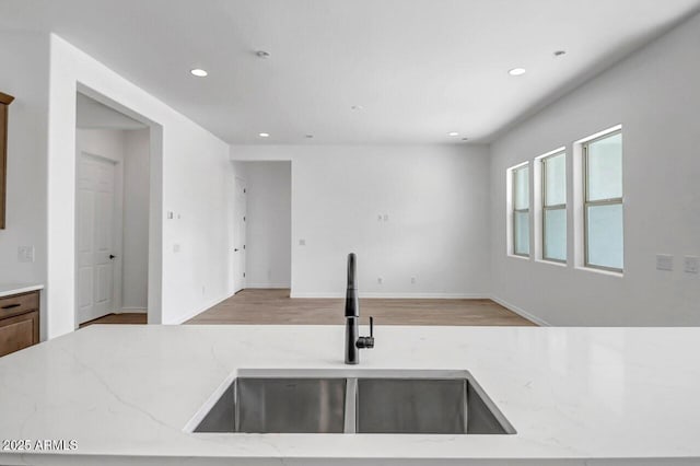 kitchen featuring light stone counters, recessed lighting, wood finished floors, and a sink