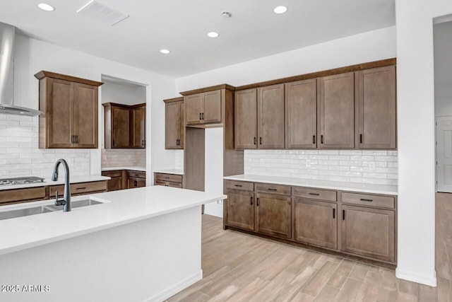 kitchen featuring light wood-style flooring, a sink, decorative backsplash, light countertops, and wall chimney range hood