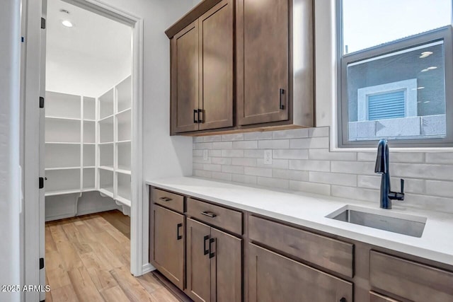 kitchen with light wood finished floors, a sink, light countertops, dark brown cabinetry, and backsplash