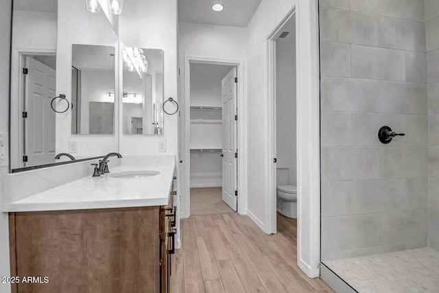 full bath featuring tiled shower, toilet, vanity, and wood finished floors