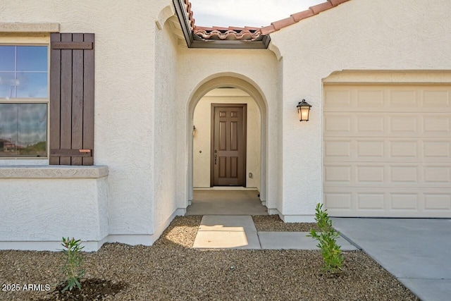 property entrance with a tile roof, an attached garage, and stucco siding