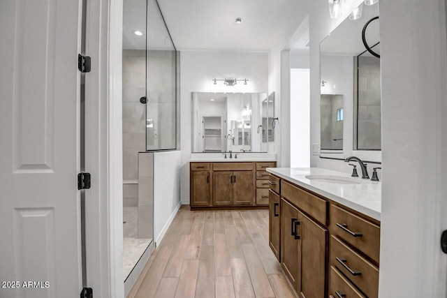 bathroom with a walk in shower, wood finished floors, two vanities, and a sink