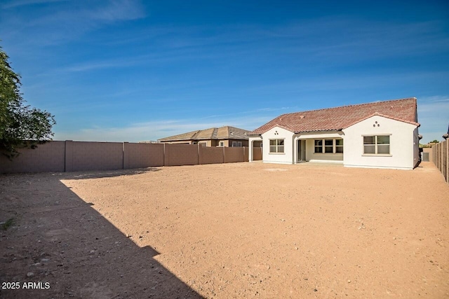 rear view of house featuring a tile roof, a fenced backyard, and stucco siding