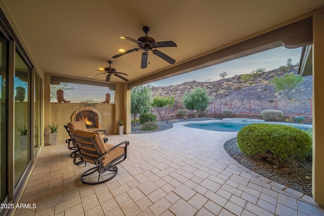 view of patio featuring a fenced in pool, ceiling fan, a mountain view, and exterior fireplace