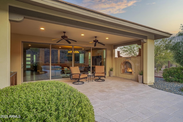 patio terrace at dusk with ceiling fan and an outdoor fireplace