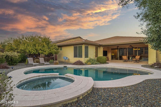 pool at dusk with an in ground hot tub, ceiling fan, and a patio area