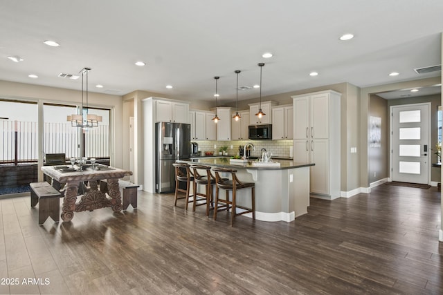 kitchen with stainless steel refrigerator with ice dispenser, a center island with sink, white cabinets, and decorative light fixtures