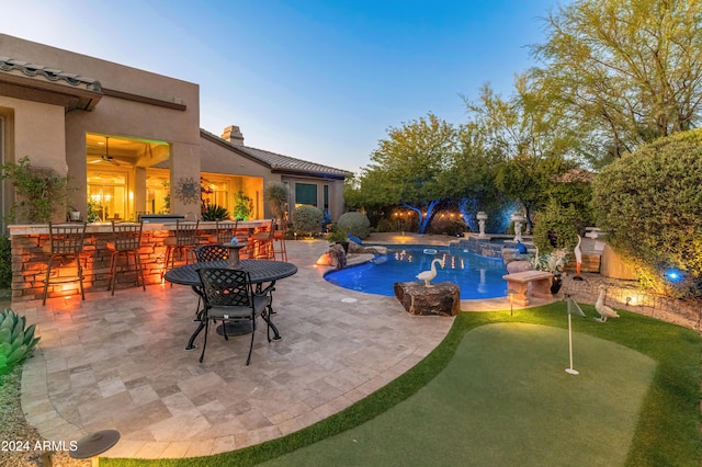 pool at dusk with a patio area and exterior bar