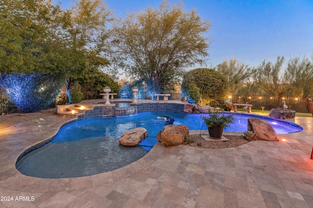 pool at dusk with pool water feature, an in ground hot tub, and a patio area