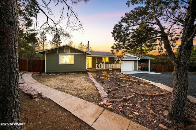 single story home featuring an attached garage, covered porch, driveway, and fence