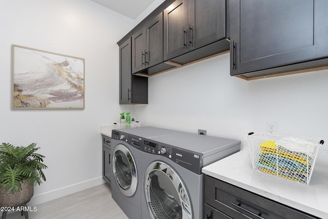 laundry area featuring washing machine and clothes dryer, cabinets, and light hardwood / wood-style floors