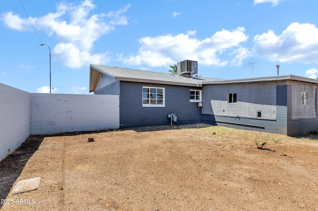 back of house with central air condition unit, fence, and concrete block siding