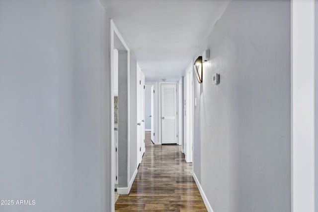 corridor featuring dark wood-type flooring and baseboards