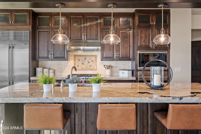 kitchen featuring backsplash, light stone counters, dark brown cabinets, and a kitchen bar