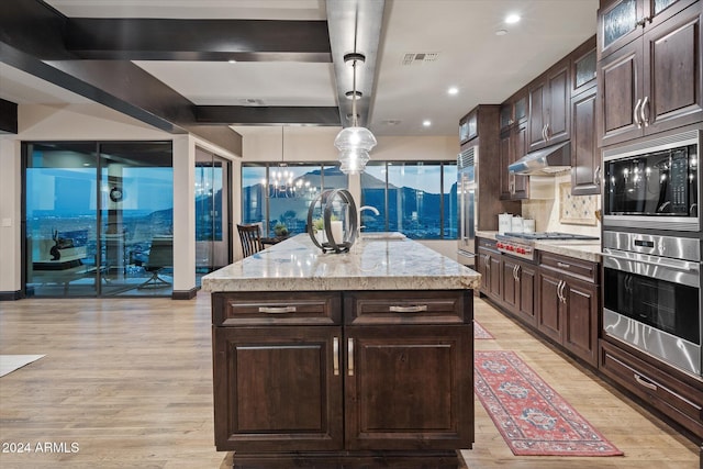 kitchen featuring built in appliances, decorative light fixtures, dark brown cabinetry, and an island with sink