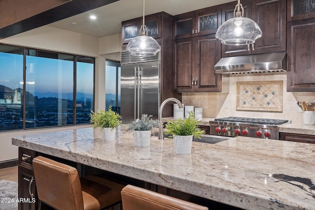 kitchen with decorative backsplash, dark brown cabinets, decorative light fixtures, and built in fridge