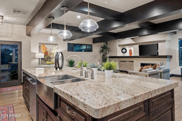 kitchen with sink, hanging light fixtures, a center island with sink, dark brown cabinets, and light wood-type flooring