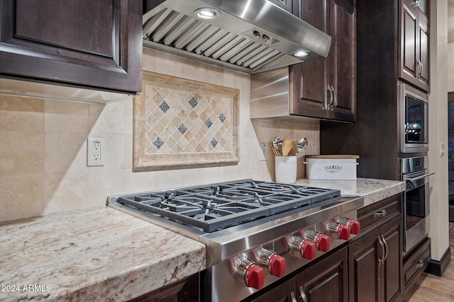 kitchen with wall chimney exhaust hood, dark brown cabinets, backsplash, and appliances with stainless steel finishes