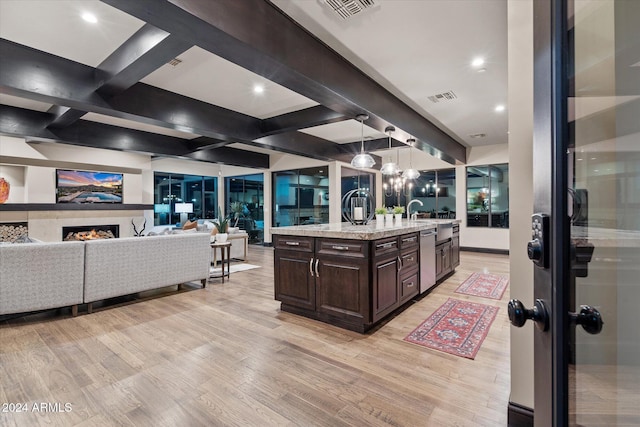 kitchen with dark brown cabinetry, beamed ceiling, light hardwood / wood-style floors, hanging light fixtures, and an island with sink