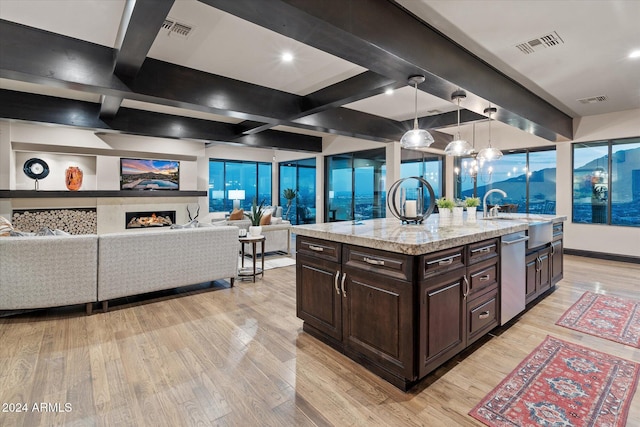 kitchen featuring light wood-type flooring, dark brown cabinetry, decorative light fixtures, dishwasher, and an island with sink