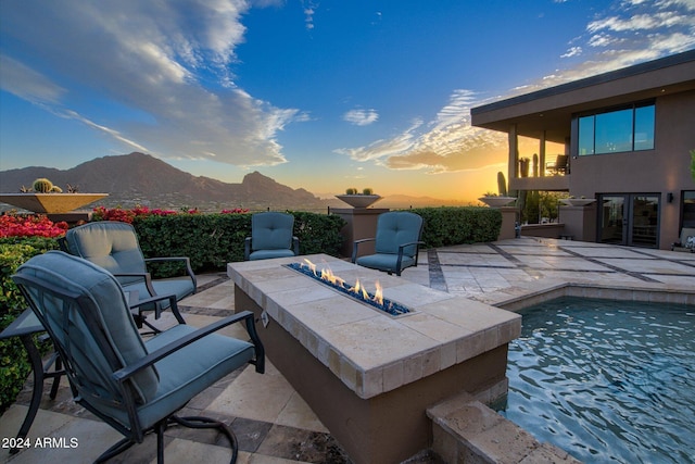 patio terrace at dusk featuring a mountain view, a balcony, and an outdoor fire pit