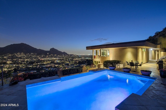 pool at dusk featuring a mountain view, a patio, and grilling area