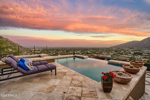 pool at dusk featuring a mountain view and a patio