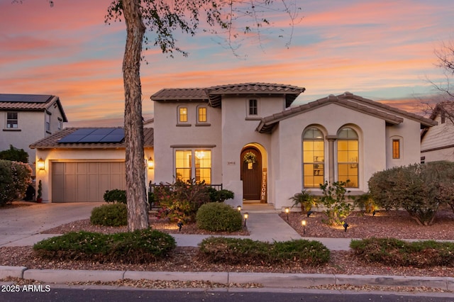 mediterranean / spanish-style home featuring a garage, solar panels, concrete driveway, a tiled roof, and stucco siding