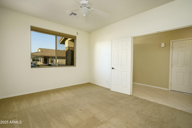 carpeted empty room with tile patterned floors, visible vents, baseboards, and ceiling fan