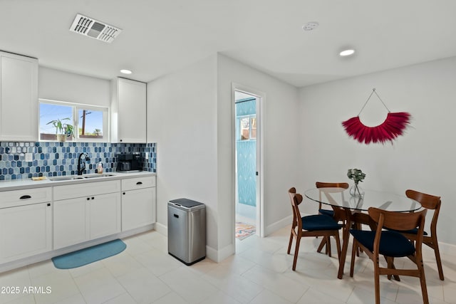 kitchen featuring tasteful backsplash, white cabinets, visible vents, and a sink