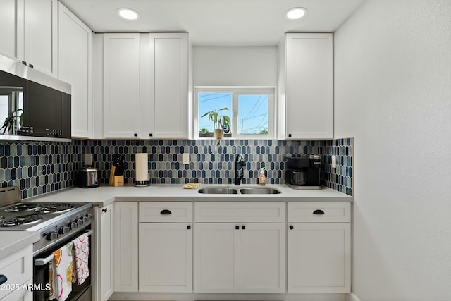 kitchen featuring decorative backsplash, stove, stainless steel microwave, white cabinetry, and a sink