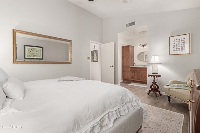 bedroom with connected bathroom, light hardwood / wood-style floors, and vaulted ceiling