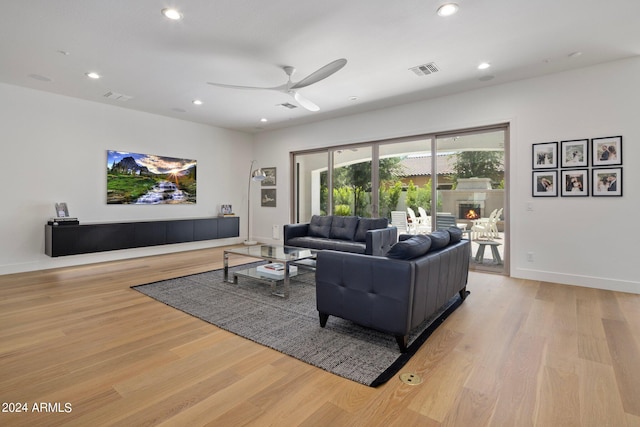 living room with light hardwood / wood-style flooring, ceiling fan, and a tiled fireplace