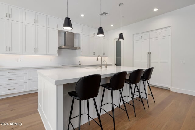 kitchen with a center island with sink, wall chimney range hood, white cabinetry, and light hardwood / wood-style floors