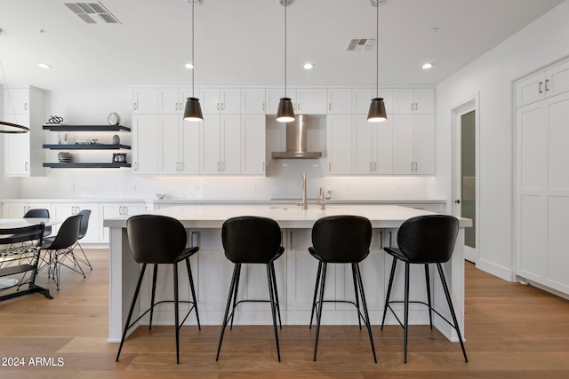 kitchen featuring a kitchen island with sink, wall chimney exhaust hood, and white cabinetry