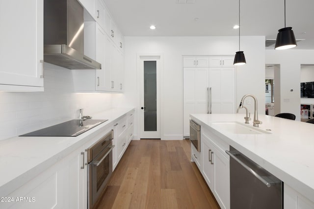 kitchen with wall chimney exhaust hood, pendant lighting, appliances with stainless steel finishes, sink, and light wood-type flooring