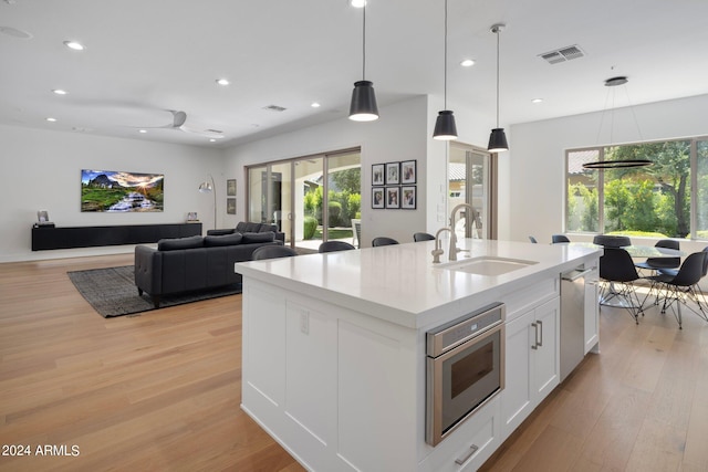 kitchen with a center island with sink, a healthy amount of sunlight, light hardwood / wood-style flooring, and white cabinets