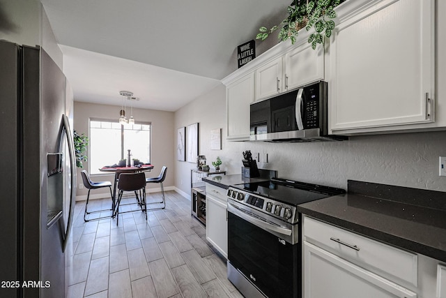 kitchen with white cabinetry, decorative light fixtures, dark stone counters, and appliances with stainless steel finishes