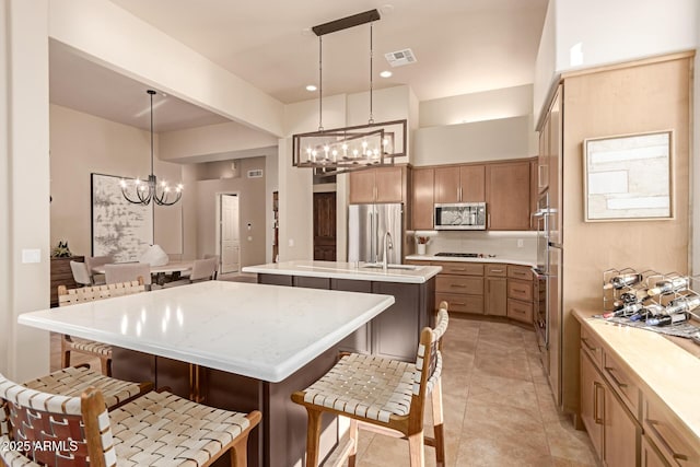 kitchen featuring hanging light fixtures, appliances with stainless steel finishes, a chandelier, and a center island with sink