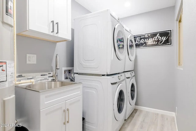 washroom with sink, cabinets, water heater, stacked washer / dryer, and light hardwood / wood-style floors