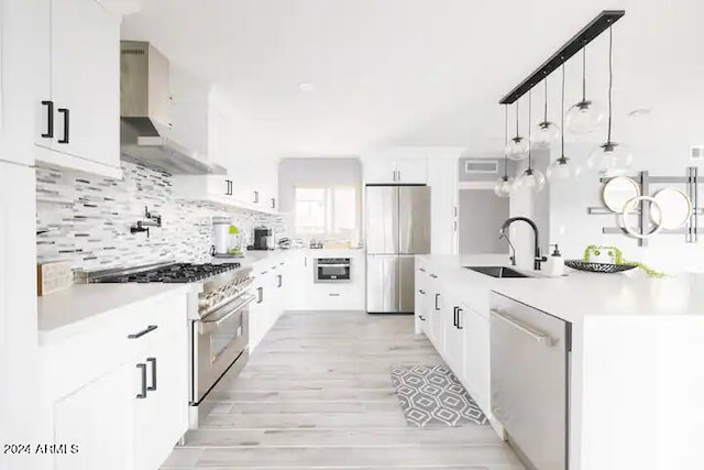 kitchen featuring wall chimney range hood, sink, hanging light fixtures, white cabinetry, and stainless steel appliances