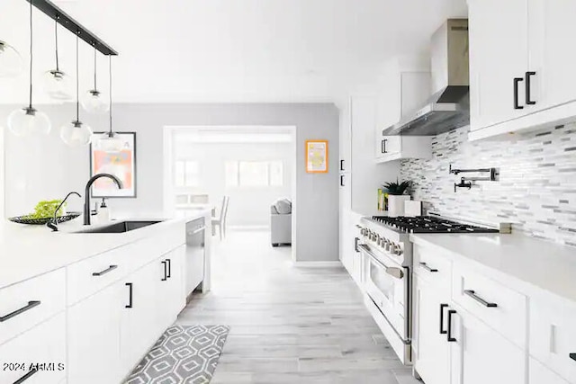 kitchen with white cabinetry, sink, wall chimney exhaust hood, stainless steel appliances, and decorative light fixtures