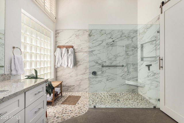 bathroom featuring a healthy amount of sunlight, a marble finish shower, and vanity
