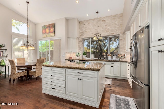 kitchen featuring tasteful backsplash, light stone countertops, high vaulted ceiling, freestanding refrigerator, and an inviting chandelier