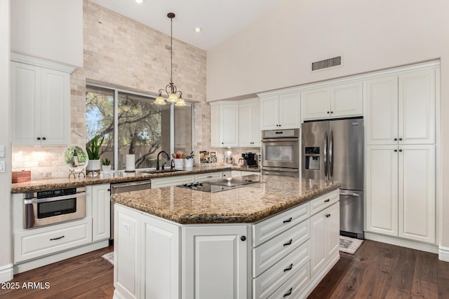 kitchen featuring decorative backsplash, visible vents, a towering ceiling, appliances with stainless steel finishes, and a sink